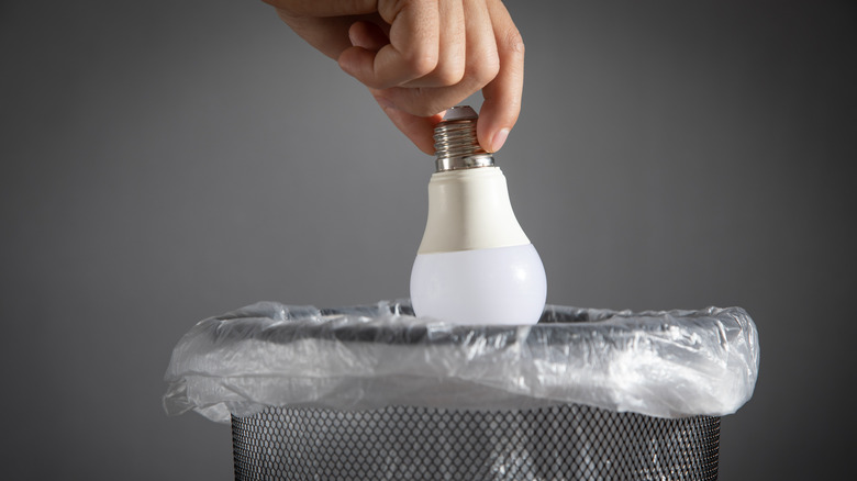 A person throwing a light bulb into a trash can