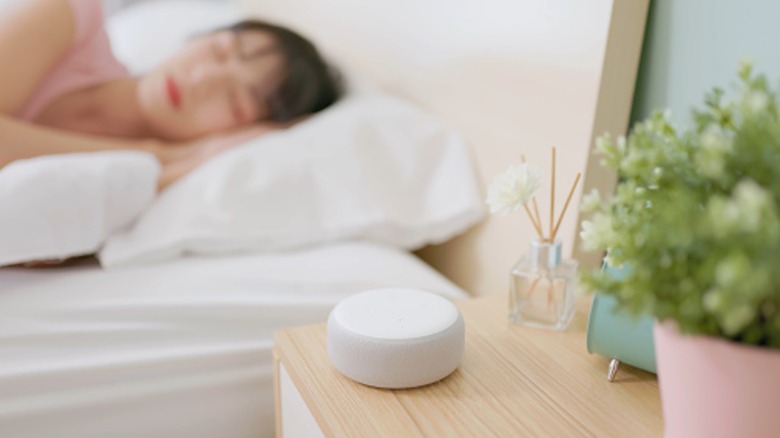 A white noise machine on a table beside a person sleeping in bed