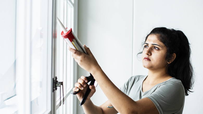 Woman applying silicone sealant to a window