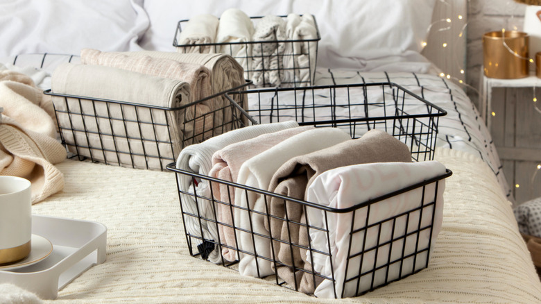 Metal storage baskets for linens are placed on white bedding