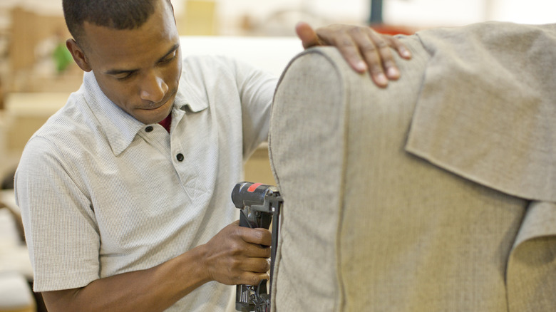 Man using staple gun on furniture to attach gray fabric