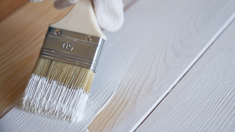 Close up of paint brush with white paint on wood.