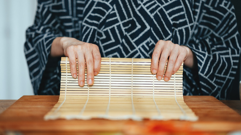 A person in a kimono holding an unfolded bamboo sushi mat.