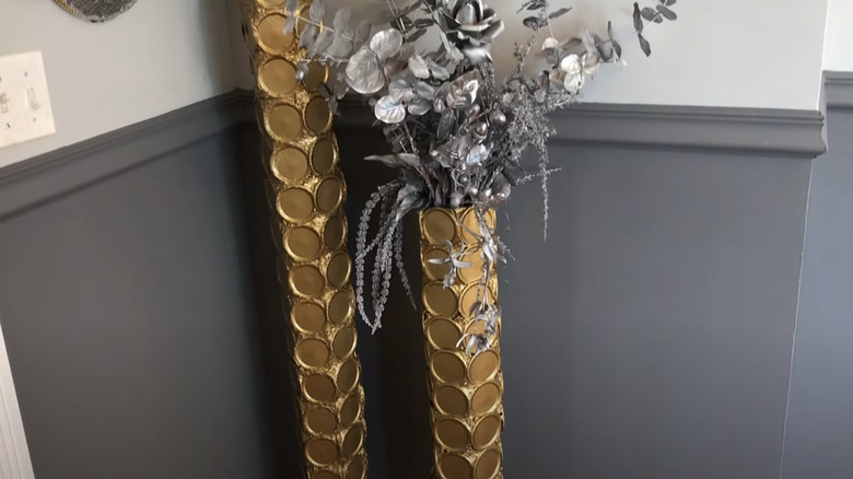 Two tall gold vases made out of shipping tubes and canning lids.