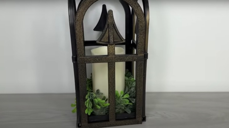 An antique-looking lantern with an LED candle and greenery in the center