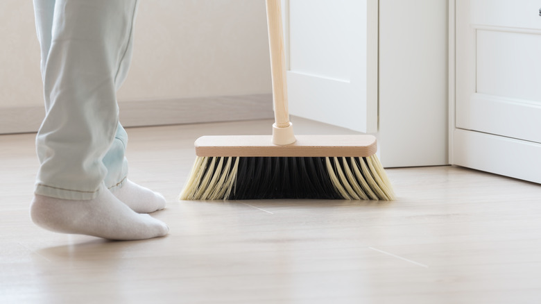 A person wearing socks holds a broom in a white room.