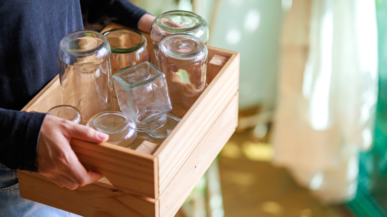 A person carrying a crate filled with empty glass jars