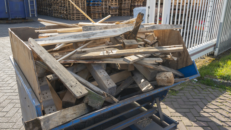 A blue dumpster is filled with scrap wood