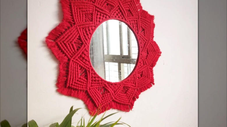 A macrame bright red mirror hangs on a wall