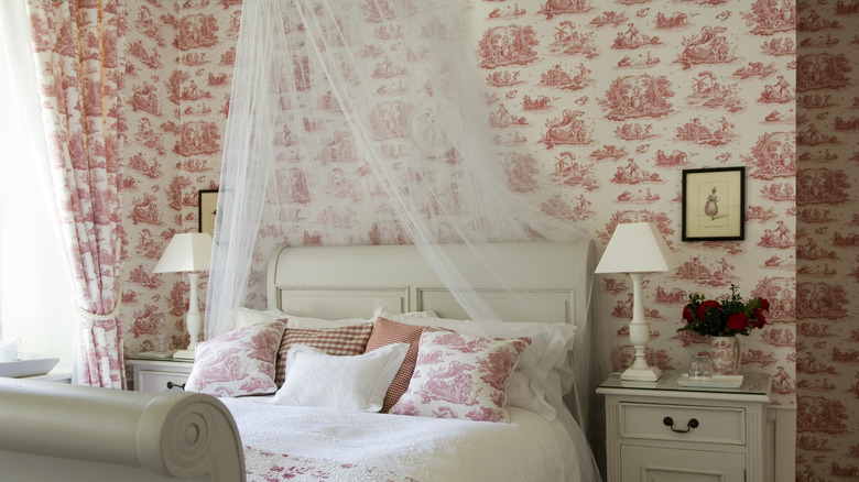 A bed with a white canopy sits in a room with red patterned wallpaper