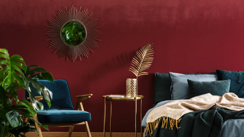 A bed with teal bedding and a teal chair sit in front of a deep red wall