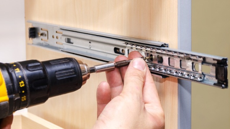 person drilling ball-bearing drawer glide into side of cabinet