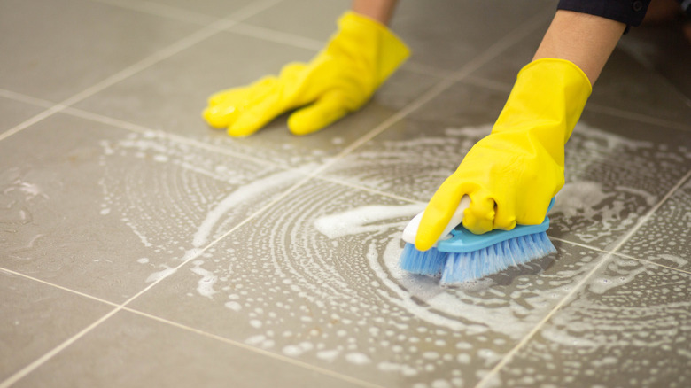 Person scrubbing tile floor with brush