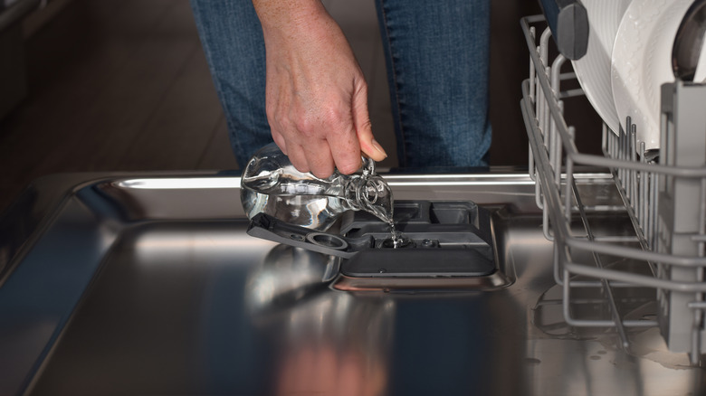 Hand pouring vinegar into dish pod compartment in dishwasher