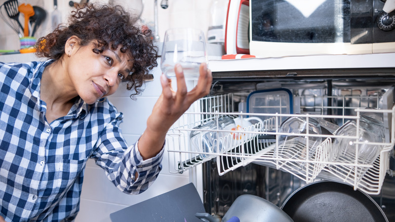 woman inspecting dirty glass in dishwasher