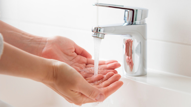 Hands testing water under the faucet