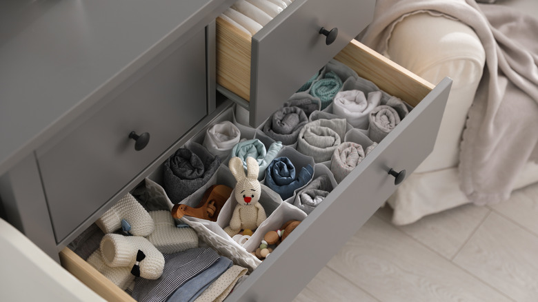 A dresser drawer is open, showing organization bins with baby clothes and accessories