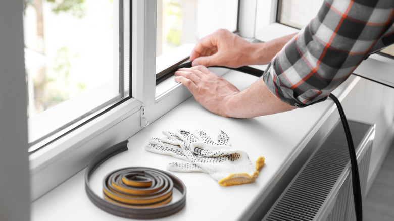 A person is sealing cracks in windows with tape.