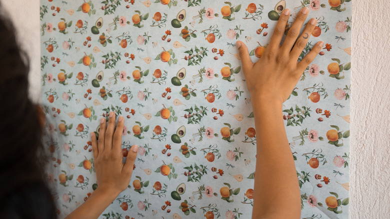 person holding wallpaper to wall