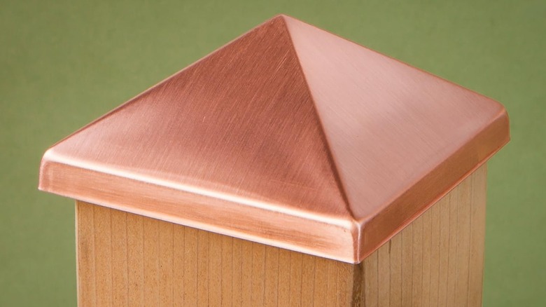 A shiny copper fence post cap is on top of a wood post