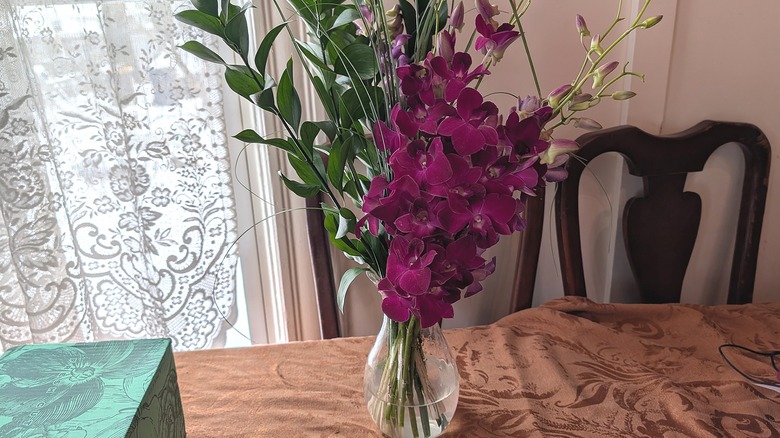 Orchids and other plants  are arranged in a vase.