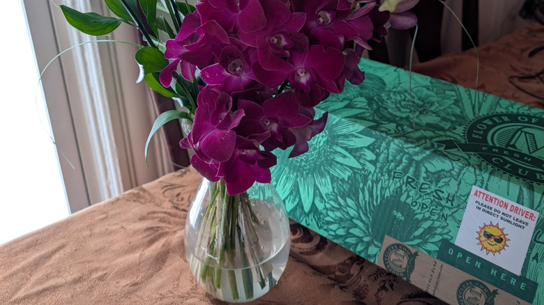 A colorful arrangement of orchids and greenery are in a vase on a table.