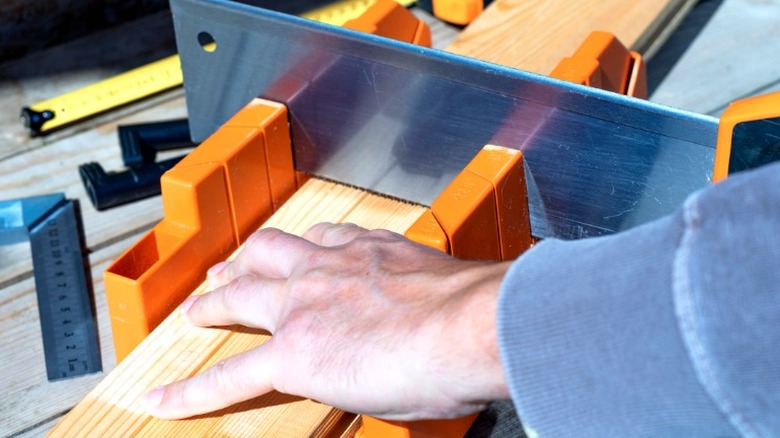 man cutting group of wood slats in miter box