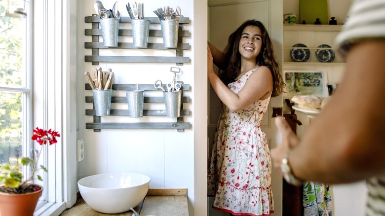 smiling woman in floral dress looking at man while reaching into kitchen pantry