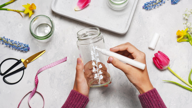 woman painting glass jar to make vase