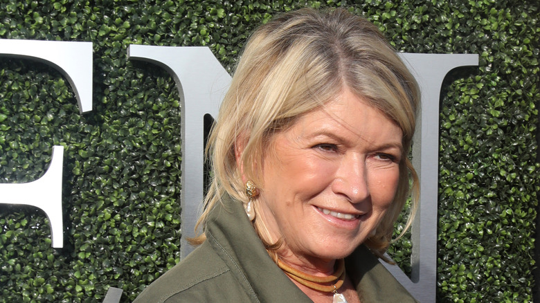 Martha Stewart smiling in front of a green hedge