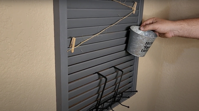 Man placing a bucket on a wood shutter entryway hanging organizer