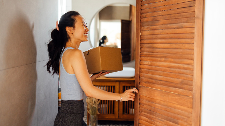 A woman opening a wood slat door in her home.