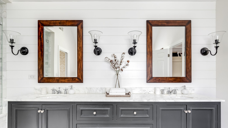 A bathroom with a double sink features four wall sconces on a shiplap accent wall.