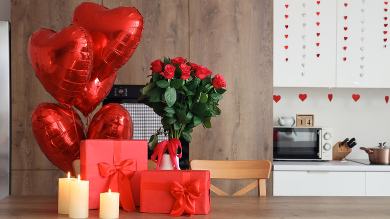 Valentine's Day balloons, roses, and gifts rest on a wood table.