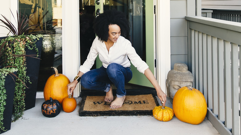 woman puts pumpkins on front porch