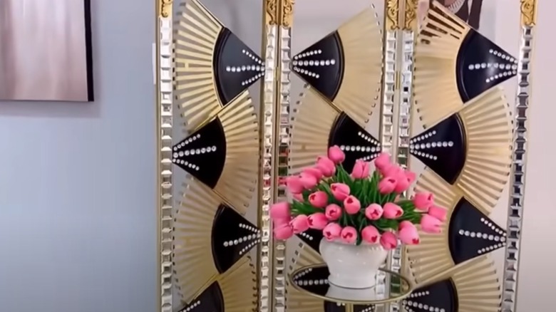 Black and gold fan room divider with crystals behind vase of roses