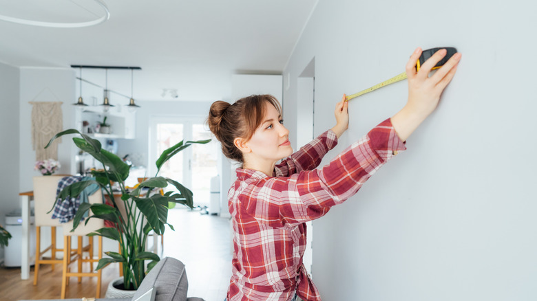 Woman measuring the wall in her living room before installing shelves