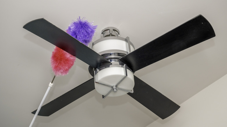 Black ceiling fan being cleaned with duster