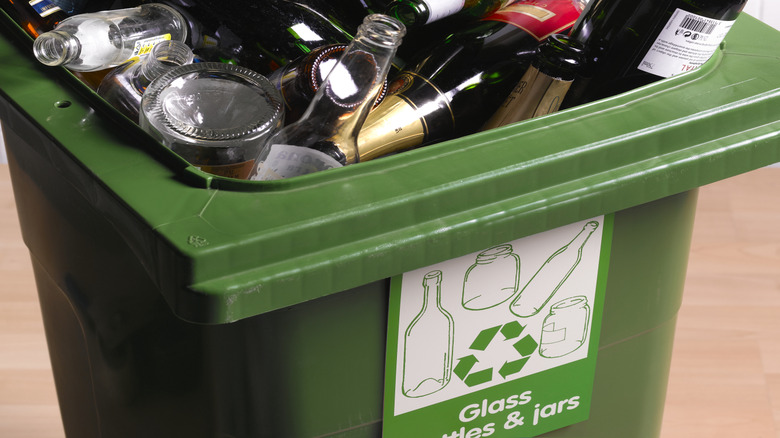 A garbage bin is overflowing with glass bottles.