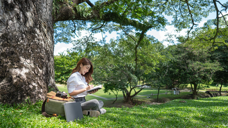 Woman sitting underneath a tree in the grass 