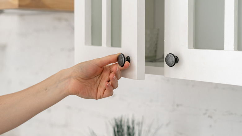 Person opening white cabinet door with black knob