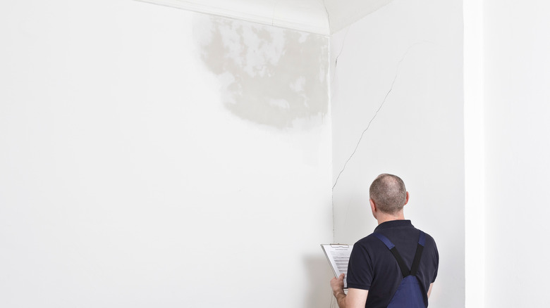 Man examining water damaged ceiling and cracks