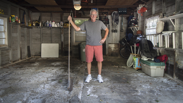 A man stands in his garage holding a broom.