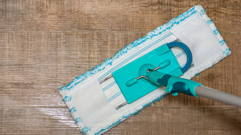 Close up image of someone mopping vinyl flooring with a white and teal mop