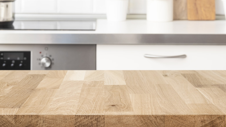 A butcher block countertop in the foreground of a white kitchen