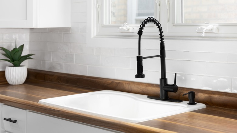 A white sink in a dark butcher block counter with a black faucet against a white backsplash