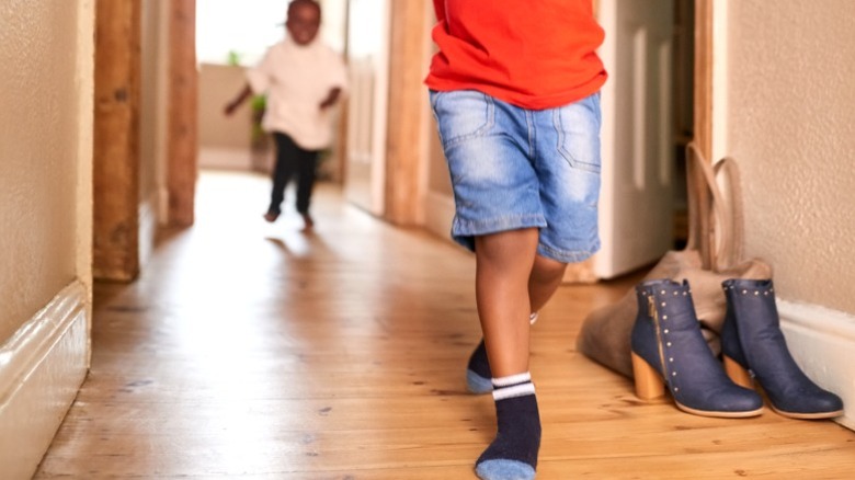 boy in socks running away from sister on hardwood floor in hallway