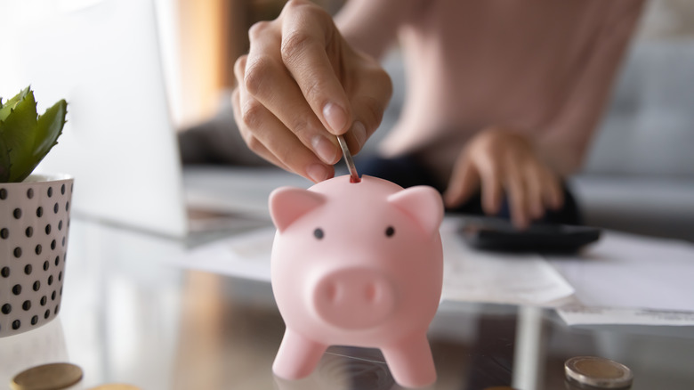 Hand puts coin in piggy bank