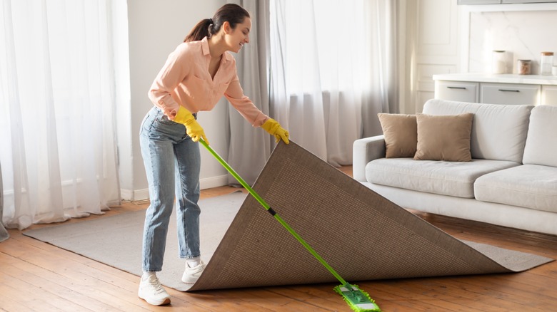 young woman scrubbing under living room rug