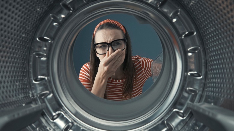 Woman with glasses holding nose and looking into washer